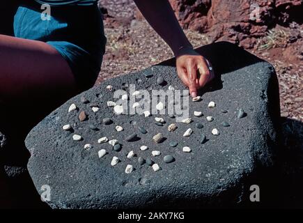 Un antico gioco Hawaiiano chiamato kōnane può essere giocato con piccoli pezzi di corallo bianco e scuro pietre di lava su un originale gameboard che è un piatto di roccia lavica trovato nel Puʻuhonua o Hōnaunau National Historical Park sulla Big Island delle Hawaii in Hawaii, Stati Uniti d'America. Ha inventato dai primi Polinesiani che si insediarono le isole hawaiane nell'Oceano Pacifico, il gioco è cominciato alternando il bianco e nero a pezzi in un modello di fori poco profonde scavate nella pietra piatta. Due giocatori poi a turno hopping oltre i pezzi dell'avversario per catturarli, come nel gioco della dama. Foto Stock