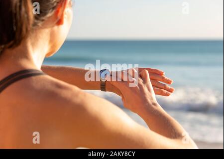 Sportivo da donna controllando il suo guardare dopo aver eseguito dal mare, vicino. Foto Stock