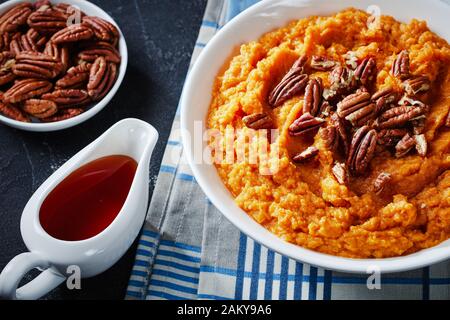 purè di patate dolci condite con noci pecan in una ciotola con sciroppo d'acero in una barca bianca su un tavolo di cemento, vista orizzontale dall'alto Foto Stock