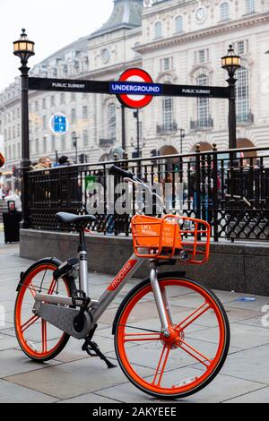 Londra, Regno Unito - 31 dicembre 2019: Condivisione di biciclette a Londra. Una bicicletta a noleggio a Piccadilly Circus con l'uscita della metropolitana e gli edifici di Londra nel retro Foto Stock