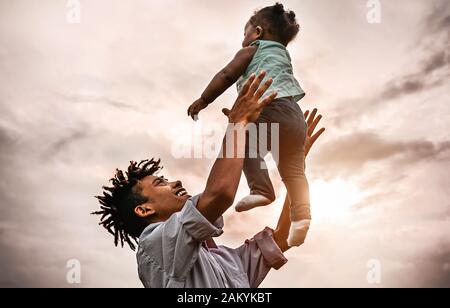 Buon padre che gioca con la sua figlia del bambino durante il tramonto - la famiglia Afro che si diverte all'aperto - Concetto di bambino, felicità e paternità Foto Stock