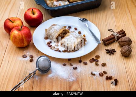 Rotolo di apple pie - Strudel di mele. Torta di mele, cannella, noci e uvetta, spolverati con zucchero a velo in un piatto su un tavolo di legno Foto Stock