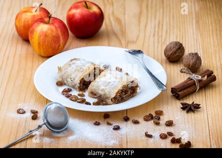 Rotolo di apple pie - Strudel di mele. Torta di mele, cannella, noci e uvetta, spolverati con zucchero a velo in un piatto su un tavolo di legno Foto Stock