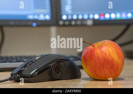 Il mouse del computer e una mela rossa su sfondo sfocato di schermo di luce. Foto Stock