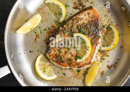 Limone aglio Pesce spada in una Skillet: Una bistecca di pesce spada fritta in salsa di burro all'aglio, guarnita con spicchi di limone e erba cipollina Foto Stock