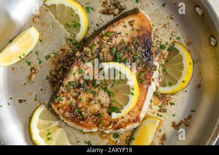 Limone aglio Pesce spada in una Skillet: Una bistecca di pesce spada fritta in salsa di burro all'aglio, guarnita con spicchi di limone e erba cipollina Foto Stock