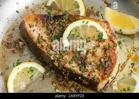 Limone aglio Pesce spada in una Skillet: Una bistecca di pesce spada fritta in salsa di burro all'aglio, guarnita con spicchi di limone e erba cipollina Foto Stock