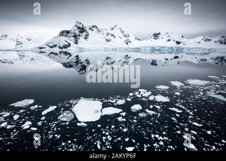 Ghiaccio del ghiacciaio, ghiaccio di cenere, iceberg di fronte alle montagne e ghiacciai della baia del Paradiso con riflessi dell'Oceano, atmosfera dell'Antartide Foto Stock