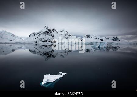Ghiaccio del ghiacciaio, ghiaccio di cenere, iceberg di fronte alle montagne e ghiacciai della baia del Paradiso con riflessi dell'Oceano, atmosfera dell'Antartide Foto Stock