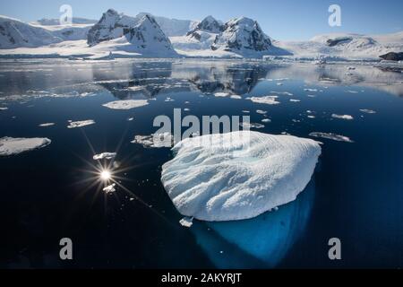 Paesaggio antartico, mare, ghiaccio, ghiacciai e montagne si riflettono nell'oceano in una luminosa giornata di sole Foto Stock