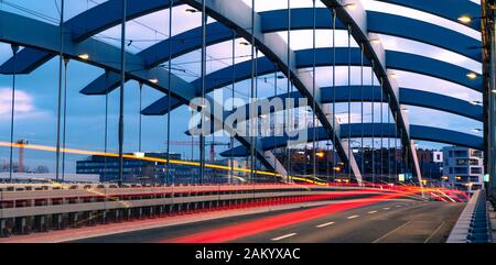 Sospensione ponte Kotlarski oltre il fiume Vistola a Cracovia, Polonia, contro la luce del tramonto. Il passaggio di vetture sentieri di luce, vista strada. Foto Stock