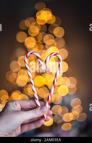 Mano che tiene due caramelle in forma di cuore con luci sullo sfondo. Foto Stock