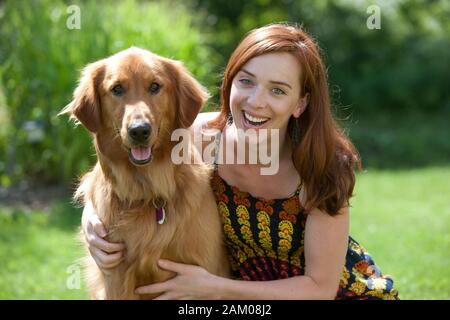 Estate ritratto di una giovane donna di posa con la tre-anno-vecchio golden retriever nel suo cortile Foto Stock