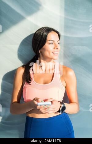 Giovane sportivo da donna seduta sul tappetino, tenendo in mano un telefono nelle sue mani, scrivere un messaggio, avente una pausa dopo la pratica dello yoga, indossare abbigliamento sportivo nero a Foto Stock