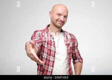 Dolce, uomo di buona natura dà la mano per handshake, guardando amabilmente la macchina fotografica. Foto Stock