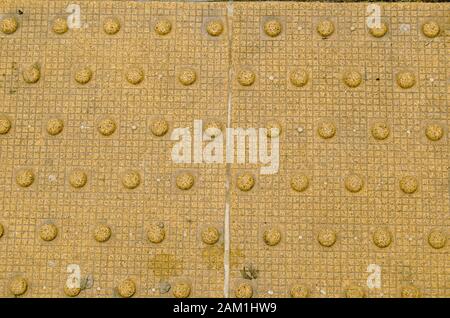 Dettaglio della pavimentazione tattile utilizzata a livello internazionale per aiutare le persone ipovedenti. Queste cupole troncate segnano il bordo di una piattaforma ferroviaria. Foto Stock