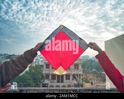 Jaipur, Rajasthan Circa 2020 - Fotografia di uomo e una signora che tiene un aquilone rosso brillante sulle loro teste con una mano ciascuno sul tetto di una ho Foto Stock