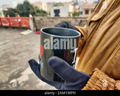 Jaipur, Rajasthan , circa 2020 - Fotografia dell'uomo che tiene una tazza nera con la bevanda calda mentre indossa i guanti sulle sue mani su giorno freddo ca. La foto Foto Stock