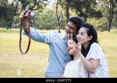 Le famiglie asiatiche stanno scattando foto di famiglia in un giardino pubblico per souvenir. I genitori e i bambini scattano foto insieme nel parco Foto Stock