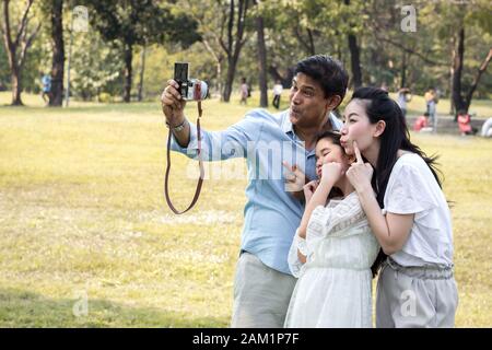 Le famiglie asiatiche stanno scattando foto di famiglia in un giardino pubblico per souvenir. I genitori e i bambini scattano foto insieme nel parco Foto Stock