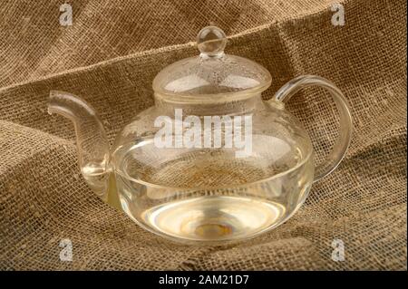 Teapot di vetro con acqua calda su uno sfondo di tessuto homespun ruvido. Primo piano Foto Stock