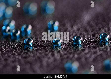 Perle di semi trasparenti di colore blu sparse su una superficie in pelle nera da vicino Foto Stock