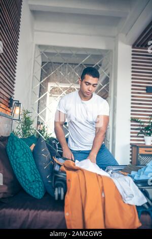 Dai capelli scuri giovane uomo in bianco tshirt cercando occupato Foto Stock