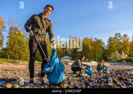 Uomo pulizia spiaggia con volontari in giornata di sole Foto Stock
