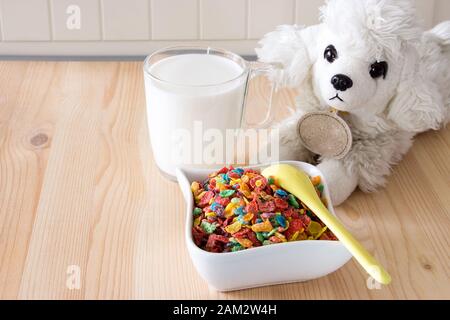 Colazione veloce e salutare per i bambini. Cereali di riso colorati, latte e cane giocattolo su sfondo di legno. Spazio di copia Foto Stock