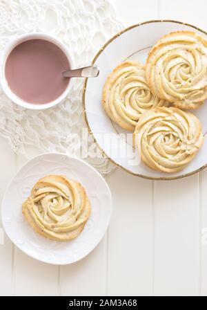 Forma rotonda di rose biscotti shortbread. Una tazza di cioccolata calda. Piatto bianco vintage e tovagliolo. Sfondo bianco in legno. Vista dall'alto. Foto con tonalità Foto Stock