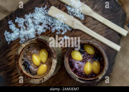 Riso cotto con latte di cocco (Khao lam) o riso glutinoso arrostito in giunture di Bambù su legno, Thai dessert concetto, vista dall'alto. Foto Stock