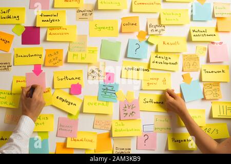 Gli uomini d'affari scrivono una nota importante, usando sul posto degli adesivi di carta. Brainstorming, lavoro di squadra. Foto Stock