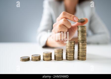 Close-up di imprenditrice mano messo monete alla pila di monete Foto Stock