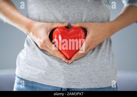 Donna incinta messa a forma di cuore con le mani Foto Stock