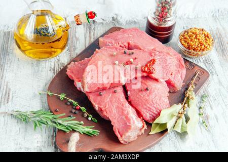 Porzioni di carne preparate per la marinatura si trovano su una tavola di argilla con spezie, olio d'oliva ed erbe aromatiche. Primo piano. Foto Stock