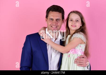 Concetto di infanzia e famiglia. Ragazza e uomo con facce sorridenti su sfondo rosa. La scolaretta si trova accanto al padre. Figlia e papà si abbracciano. Foto Stock