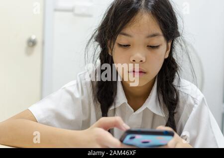 Giovani schoolgirl addicted a telefonino giochi. Fa di lui non è interessato a fare i compiti. Foto Stock