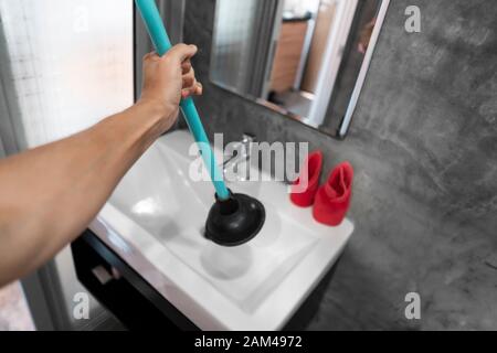 Lavandino riparare a mano con un wc stantuffo. Impianti idraulici. Un idraulico utilizza uno stantuffo per pulire un lavandino. Servizi igienici stantuffo. Foto Stock