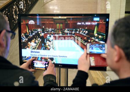 I giornalisti di guardare un feed dal vivo su una televisione che mostra la elezione di altoparlanti all'Assemblea dell'Irlanda del Nord presso gli edifici del Parlamento europeo, Stormont, Belfast, Irlanda del Nord, come la condivisione di potenza complessivo in Irlanda del Nord è stato ripristinato. Foto Stock