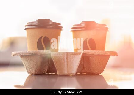 Due tazze di carta da caffè con corone nella confezione si alzano contro un tramonto sfocato al sole. Il concetto dell'inizio della giornata Foto Stock
