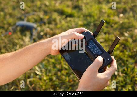 L'uomo tiene nelle sue mani un telecomando con drone. Quadcopter è a terra pronto per andare e volare sfocato sullo sfondo. Il pilota sta per iniziare Foto Stock
