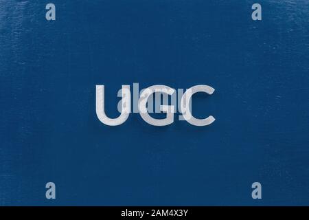 la parola ugc - contenuto generato dall'utente - posta da lettere di metallo argento bianco su sfondo blu classico in composizione centrale piatta. Foto Stock