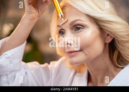 Rilassata donna matura applicando un massaggiatore wand Foto Stock