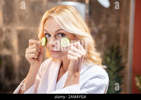 Donna applicando le fette di cetriolo per la sua guance Foto Stock