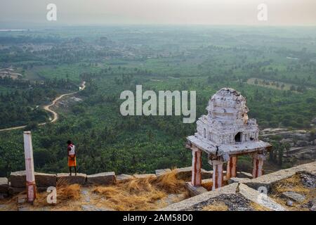 Il custode di un piccolo tempio si trova sul bordo di una collina. Centro Sacro. Il Gruppo dei Monumenti di Hampi fu il centro dell'Hindu Vijayanagara Foto Stock