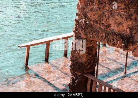 Piccola vecchia casa in pietra parzialmente sommersa con livelli d'acqua che si innalzano dal fiume. Fiume azzurro freddo. Pericolo di inondazioni che potrebbero provocare la fusione della neve Foto Stock