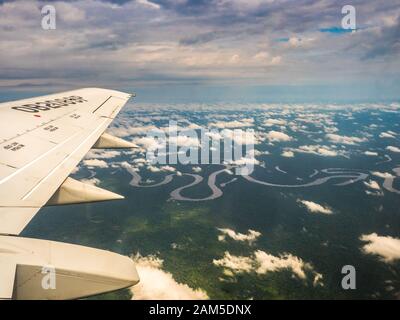 Vista dalla finestra di aereo. Ala di un aeroplano che vola sopra le nuvole oltre il fiume del Amazon. Vista superiore della foresta pluviale amazzonica. Il Perù, Brasile. La Colombia. Foto Stock