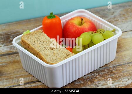 Portavivande sano e confezionato con sandwich di formaggio marrone, pepe giallo croccante e frutta fresca in scatola di plastica bianca Foto Stock