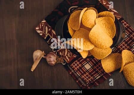 Patatine croccanti in ciotola e aglio su sfondo di legno, con asciugamano da cucina Foto Stock