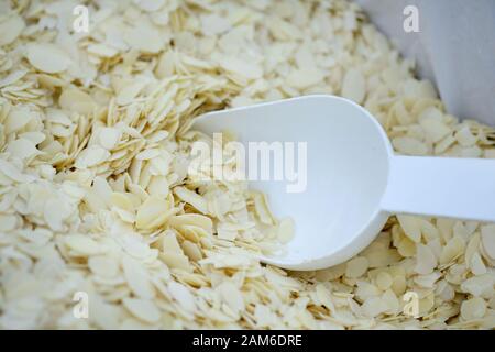 Scaglie di mandorle in una scatola con una paletta bianca in plastica. Petali di mandorle bianche in peso. Foto Stock